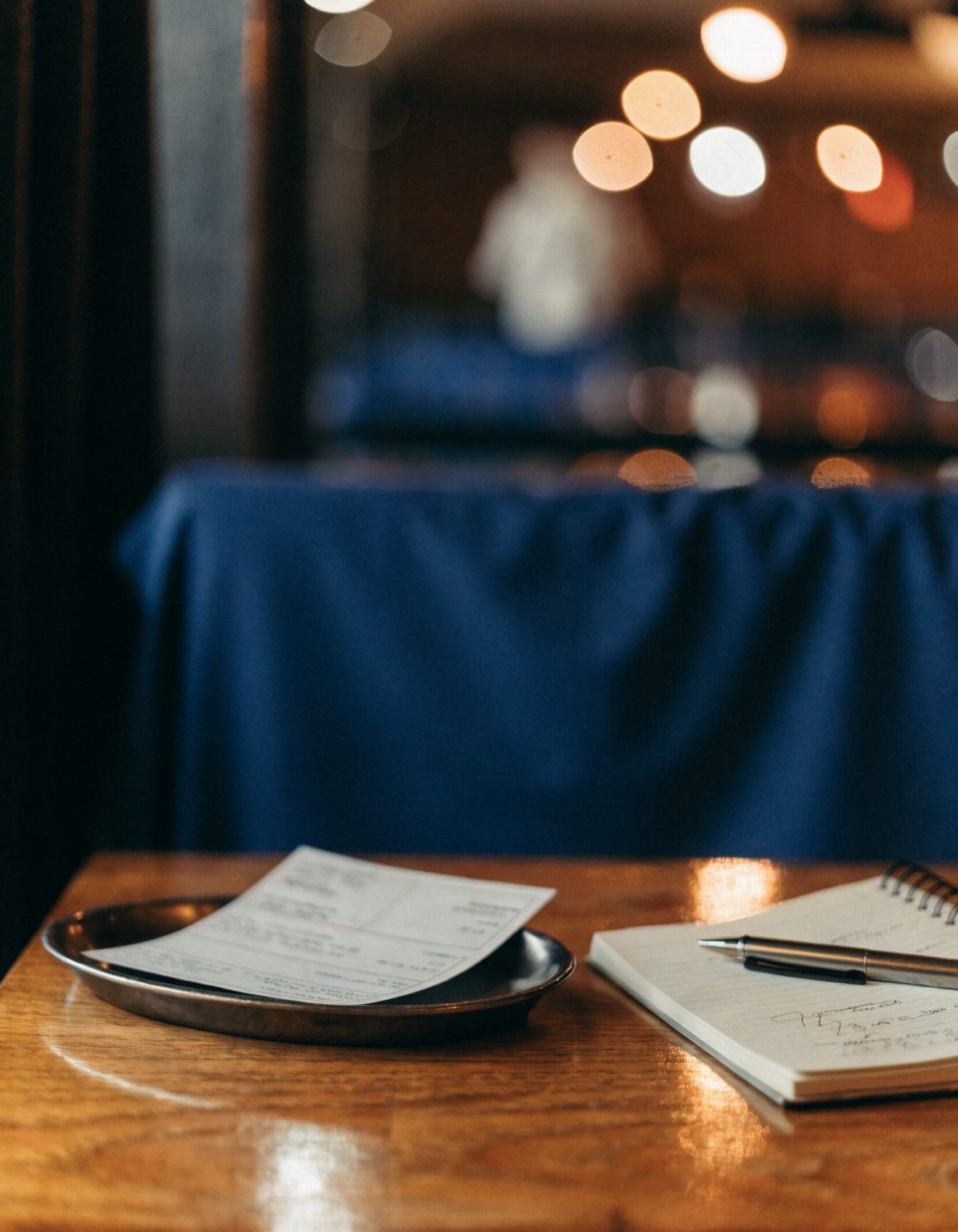 Restaurantrechnung und Notizblock Restaurantrechnung auf einem Tablett, daneben ein aufgeschlagener Notizblock mit Stift – KI-generiertes Symbolbild