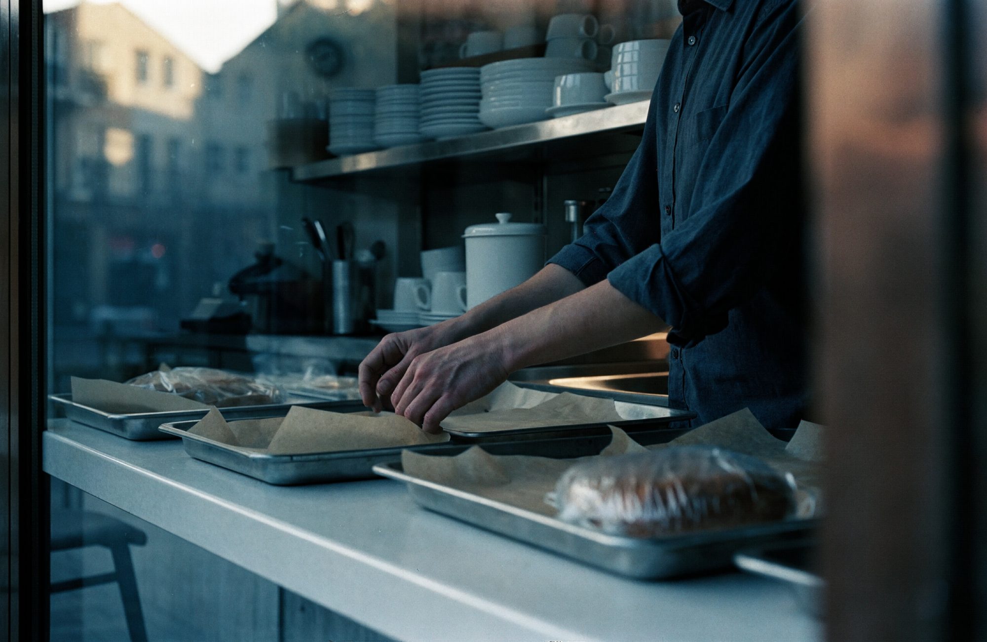 Bäckereitheke am Morgen Mitarbeiterin richtet am Morgen Bleche hinter einer Bäckereitheke – KI-generiertes Symbolbild