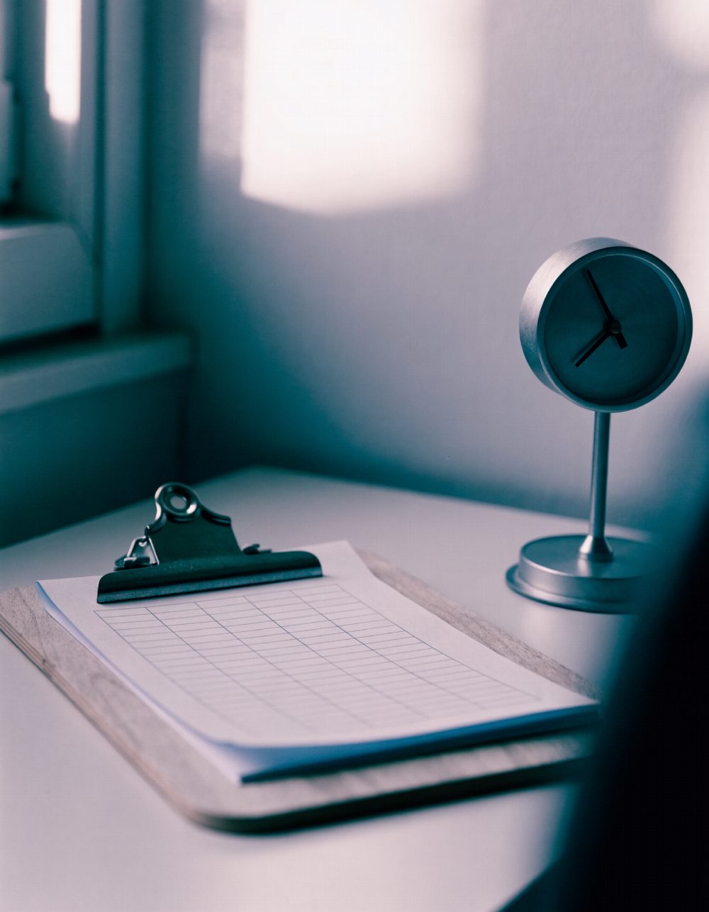 Stundenzettel und Uhr auf einem Schreibtisch Leerer Stundenzettel auf einem Klemmbrett neben einer Tischuhr – KI-generiertes Symbolbild